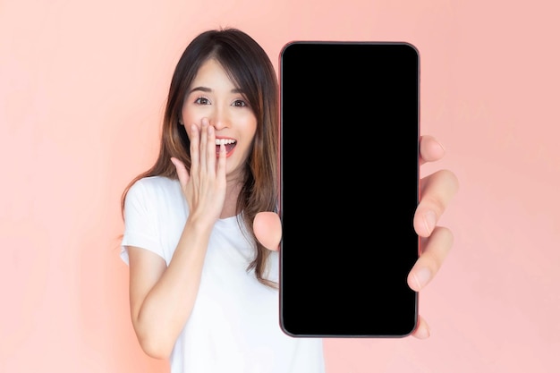 Foto bella giovane donna asiatica che mostra grande smart phone con schermo bianco schermo vuoto spazio copia vuoto per banner pubblicitario isolato su sfondo rosa mock up image