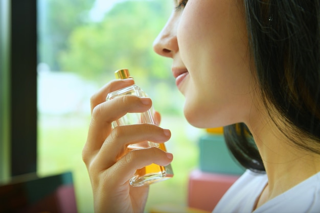 Bella giovane donna asiatica con una bottiglia di profumo in casa, primo piano