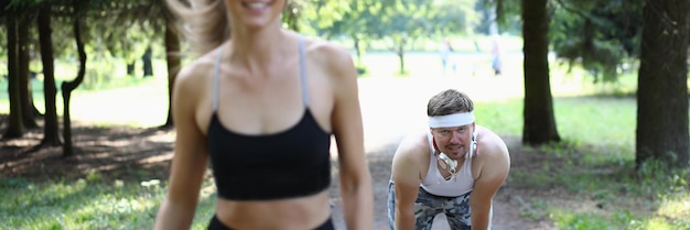 Beautiful athlete woman and tired man behind in park on jog