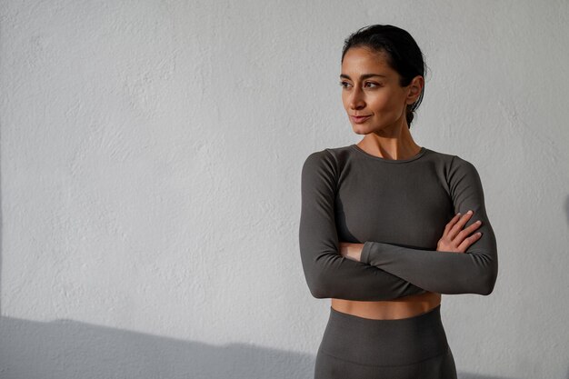 A beautiful athletic brunette in a sports suit against a white wall Sport fitness point healthy lifestyle