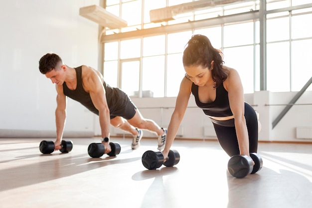 beautiful athletic couple in sportswear in training do pushups with dumbbells in the fitness room