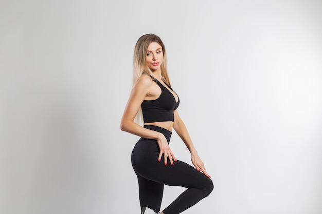 Beautiful athletic fitness woman blonde in fashionable black sportswear posing on a white background