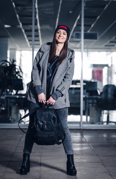Beautiful athletic girl with dark hair, a bennie, hoddie and a backpack on the gym