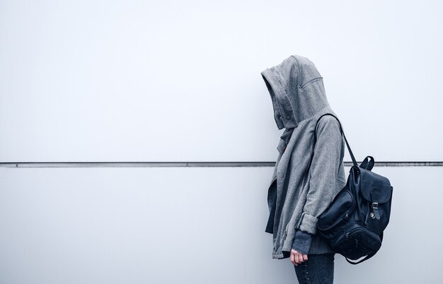 Beautiful athletic girl with dark hair a hoodie and a backpack on white wall background