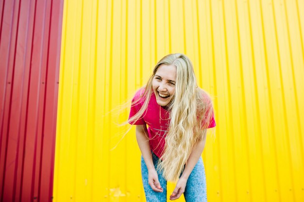 Beautiful athletic young woman with long blond hair on yellow wall.