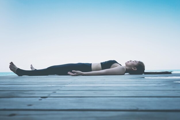 Photo beautiful attractive asian woman relaxing in yoga savasana or dead body pose to meditation warm up her muscle on beach in maldives with seasidefeeling so comfortable and relax in holidayvintage tone