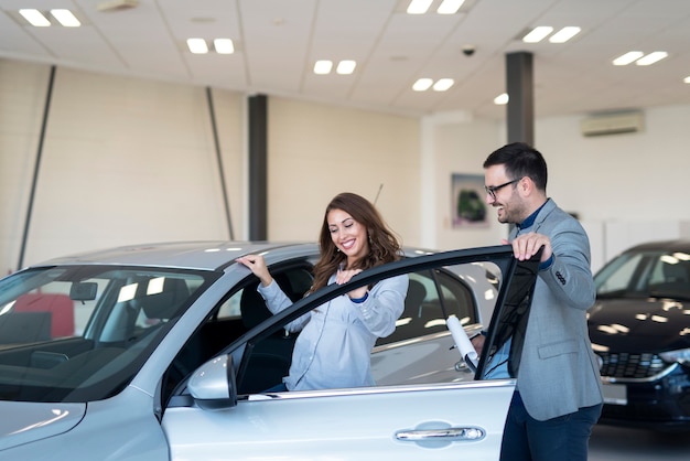 Beautiful attractive brunette entering new car at vehicle dealership.