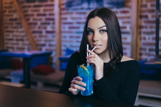 Beautiful attractive brunette young woman drinking blue lagoon cocktail in night club.