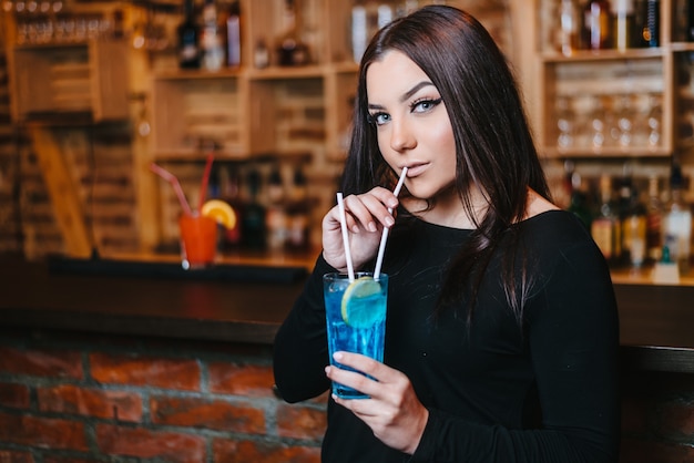 Beautiful attractive brunette young woman drinking blue lagoon cocktail in night club.