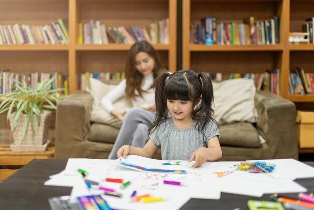 Beautiful attractive caucasian child girl doing painting with mother read book behind house family ideas concept