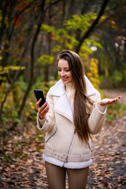 電話で美しい魅力的な女性秋の公園で selfie を作るかなり若い女性