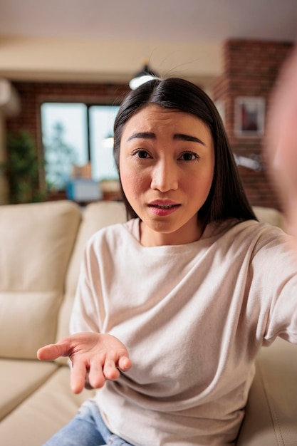 美しい本物のアジアのフィリピン人のchinesseの女性が居間で電話をかけ、カメラに挨拶する電話を持っています。オンラインウェブ技術レジャーコミュニケーションウェブカメラチャットビデオ通話