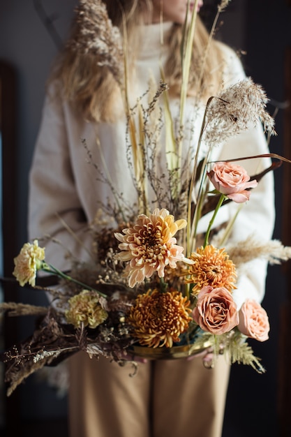 Beautiful autumn bouquet of mixed flowers with dry winds in the hands of a woman. 