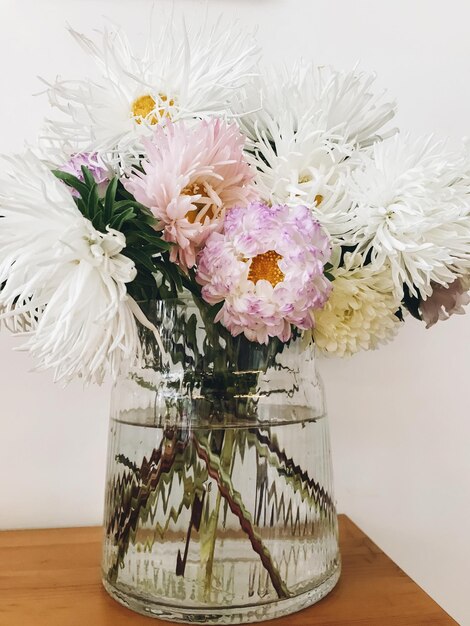 Красивые осенние цветы в современной стеклянной вазе на деревянном столе Астры и хризантемы