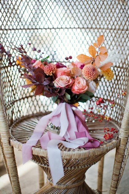 Beautiful autumn wedding bouquet with orange and red flowers and berries Autumn bouquet with ribbons on a rattan peacock chair