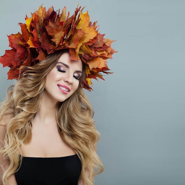 Beautiful autumn woman in autumn leaves crown on gray background