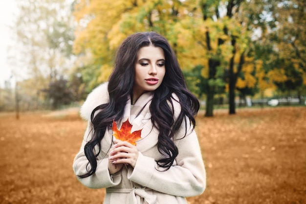 Beautiful autumn woman brunette with red maple leaf outdoors in fall park