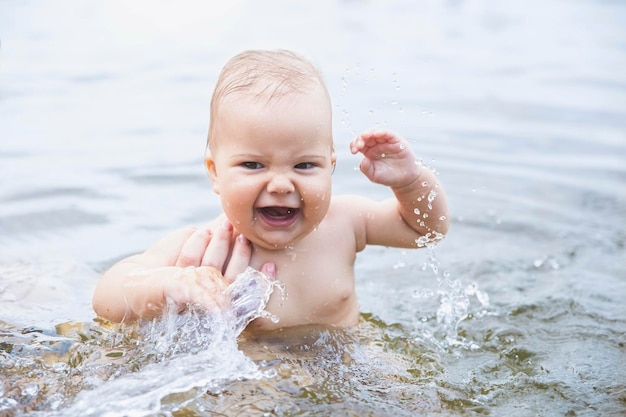 beautiful baby bathes splashing water and laughing and mom supports daughter by hand