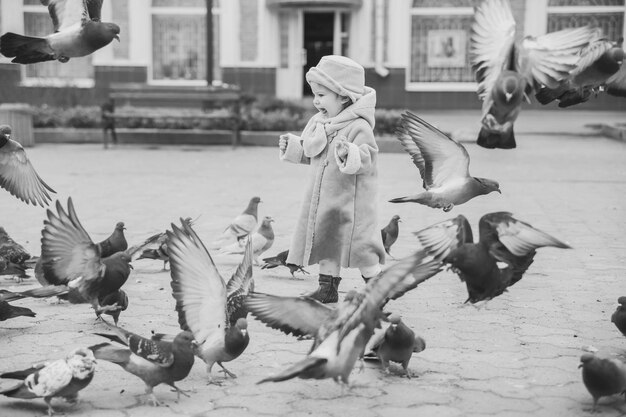 Beautiful baby in coat rejoices in pigeons