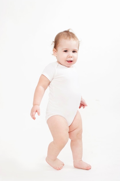 Beautiful baby dressed in white walking on a white background