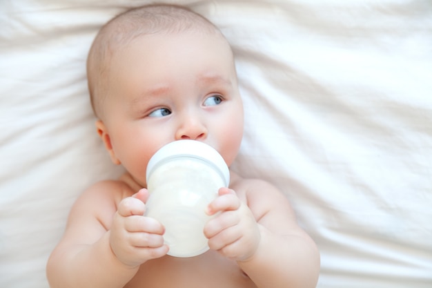 Beautiful baby eating milk from bottle on the bed