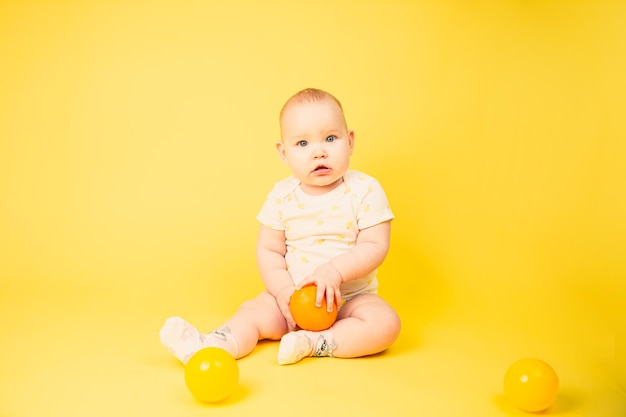 Photo beautiful baby girl holds orange sitting in studio on yellow background