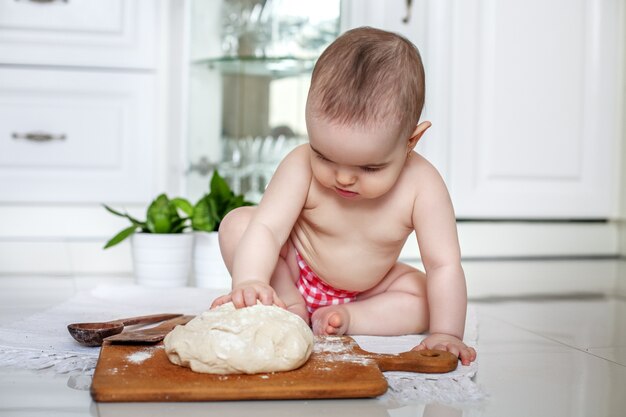 Beautiful baby girl make rolls of dough in the kitchen