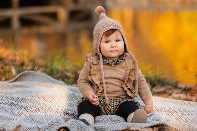 Beautiful baby girl sitting on the plaid near the pond