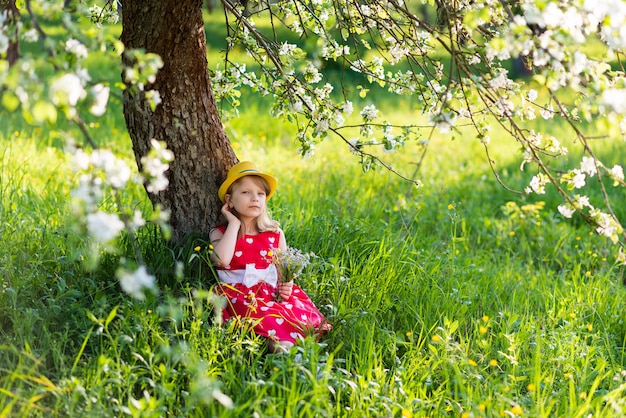 Beautiful baby girl sitting under a tree with a bouquet of wildflowers in her hands