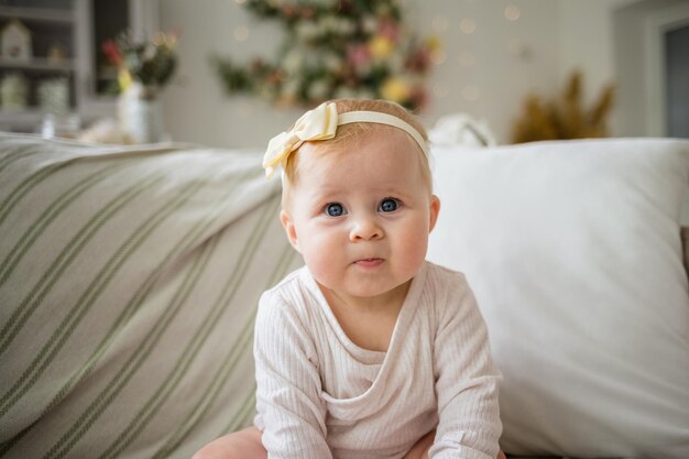 Foto bella bambina in un body bianco e una fascia è seduta sul divano nella stanza