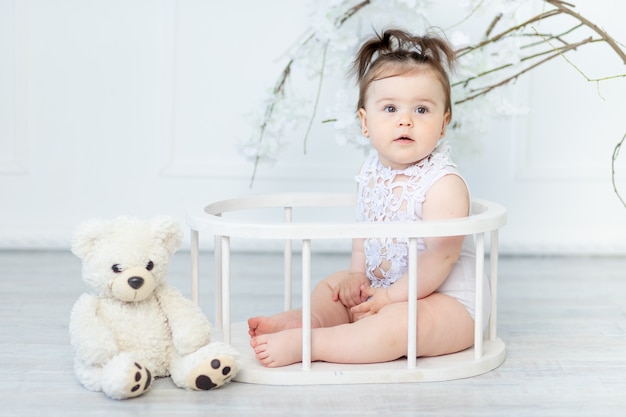 Beautiful baby girl in a white bodysuit with a teddy bear