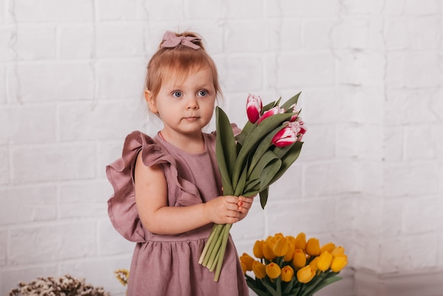 Beautiful baby girl with a bouquet of tulips on a white surface