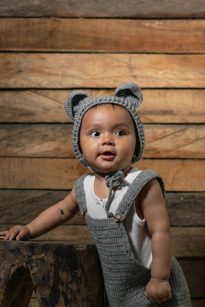 Beautiful baby latina with brown skin standing on a wooden chair and an orange background