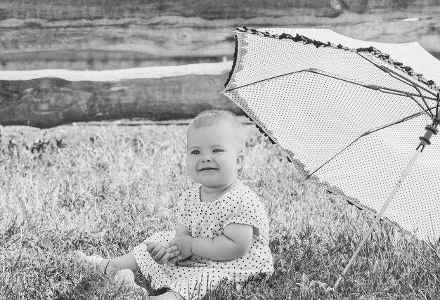 beautiful baby in a polka-dot dress is sitting nea umbrella umbrella