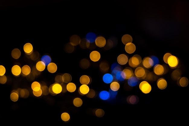 Bellissimo sfondo di cerchi rotondi blu e gialli lucidi sfocati isolati su sfondo nero, bokeh festivo per il nuovo anno, natale. striscia orizzontale di bokeh brillante blu e giallo