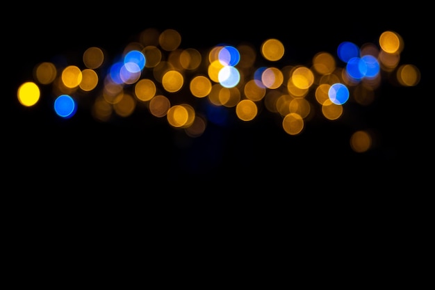 Beautiful background of defocused shiny blue and yellow round circles isolated on black background. Horizontal stripe of blue and yellow shiny bokeh to blend with your photos