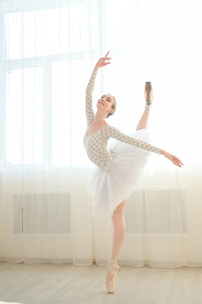 Beautiful ballerina in body and white tutu is training in a dance class Young flexible dancer posing in pointe shoes