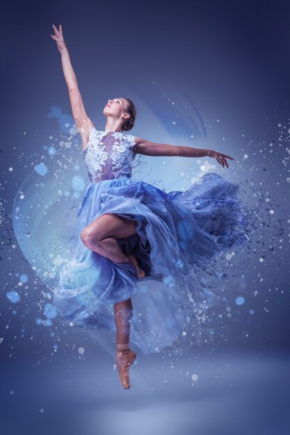 The beautiful ballerina dancing in long blue dress on blue surface