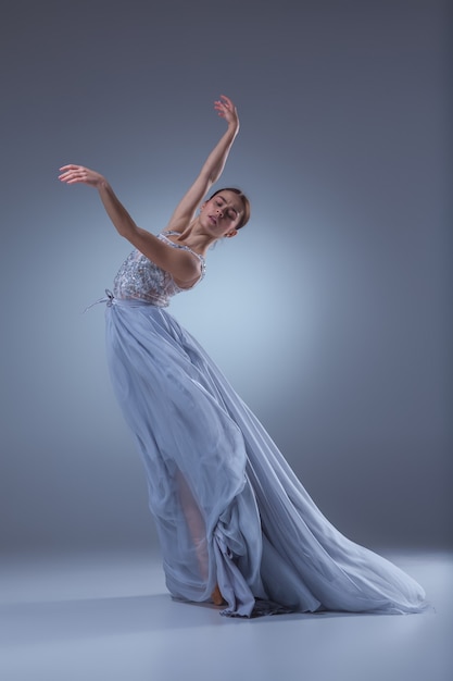 The beautiful ballerina dancing in long lilac dress on lilac background