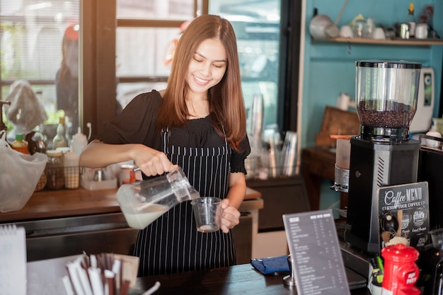 美しいバリスタは彼女のコーヒーショップで笑っています。