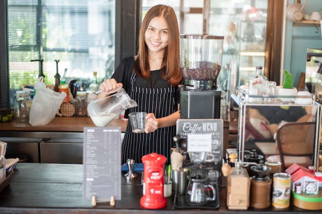 美しいバリスタは彼女のコーヒーショップで笑っています。