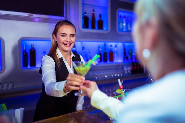 Beautiful bartender serving cocktail to woman