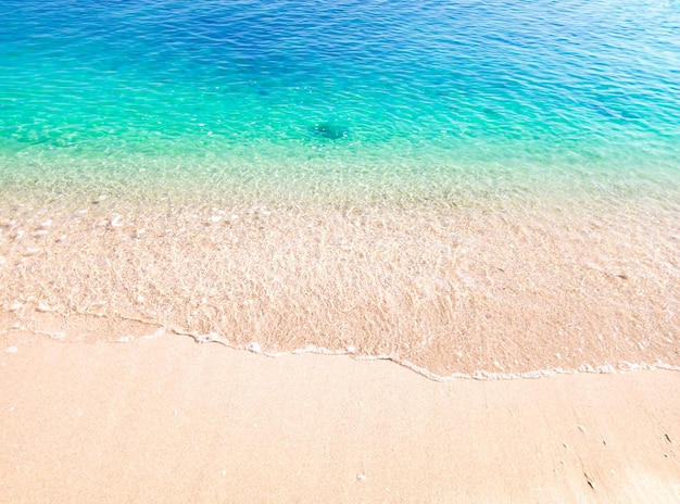 Beautiful beach background with clear and foamy blue sea water waves and clean white sandy beach.