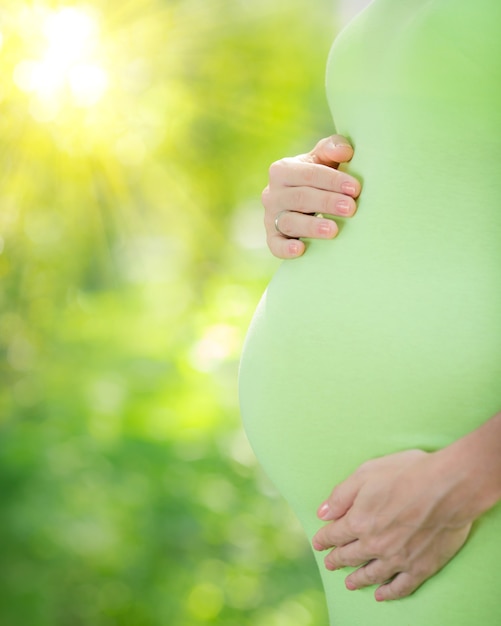 Beautiful belly of young pregnant woman against green spring background