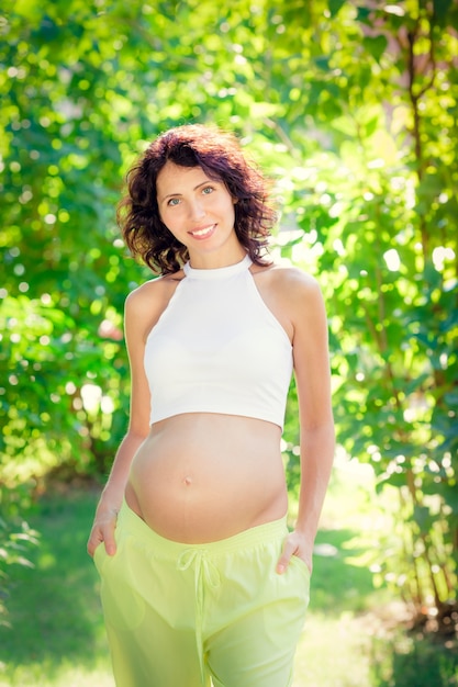 Beautiful belly of young pregnant woman against green spring background