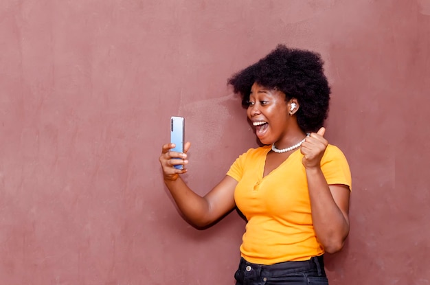 美しい黒人のアフリカ系アメリカ人女性は、携帯電話を持ち、見ながら、興奮して幸せを感じています