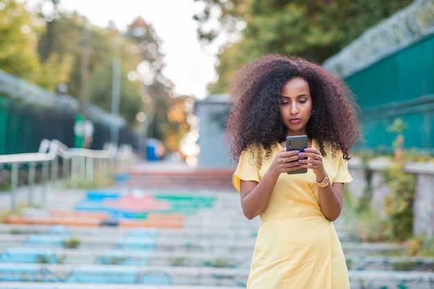 Красивая чернокожая афро женщина с серьезным и уверенным выражением лица смотрит на свой мобильный телефон.
