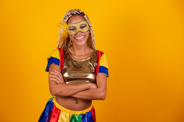 Beautiful black Brazilian woman dressed in carnival clothes mask yellow background crossed arms