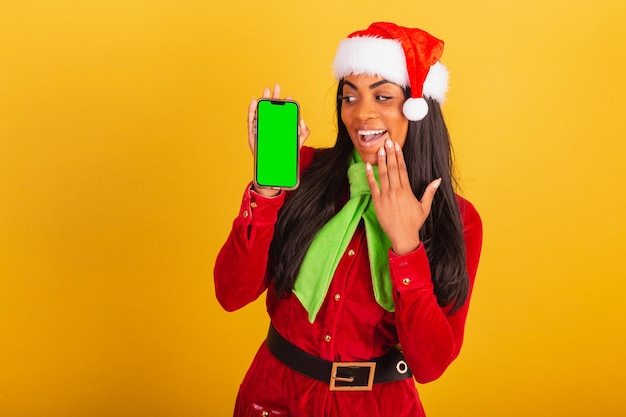 Beautiful black brazilian woman dressed in christmas clothes santa claus smartphone and showing green chroma screen