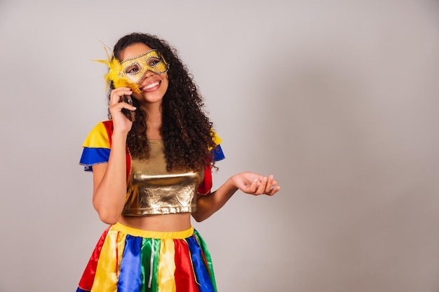 Beautiful black brazilian woman wearing carnival clothes on\
voice call with smartphone